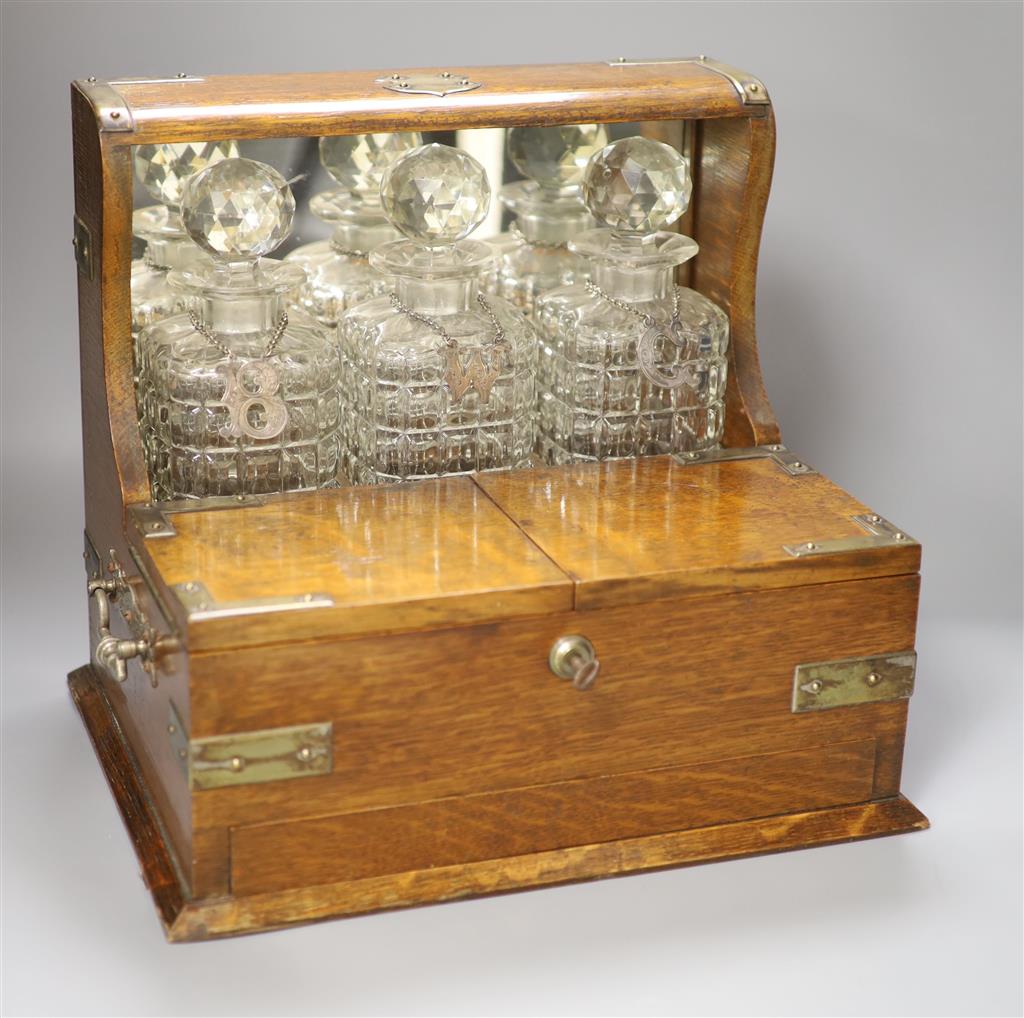 A late Victorian oak and electroplate mounted three decanter tantalus, with wine labels B, W and C